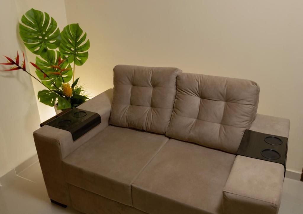 Un divano beige con un piano cottura integrato, appoggiato su un muro spoglio con una grande pianta verde.