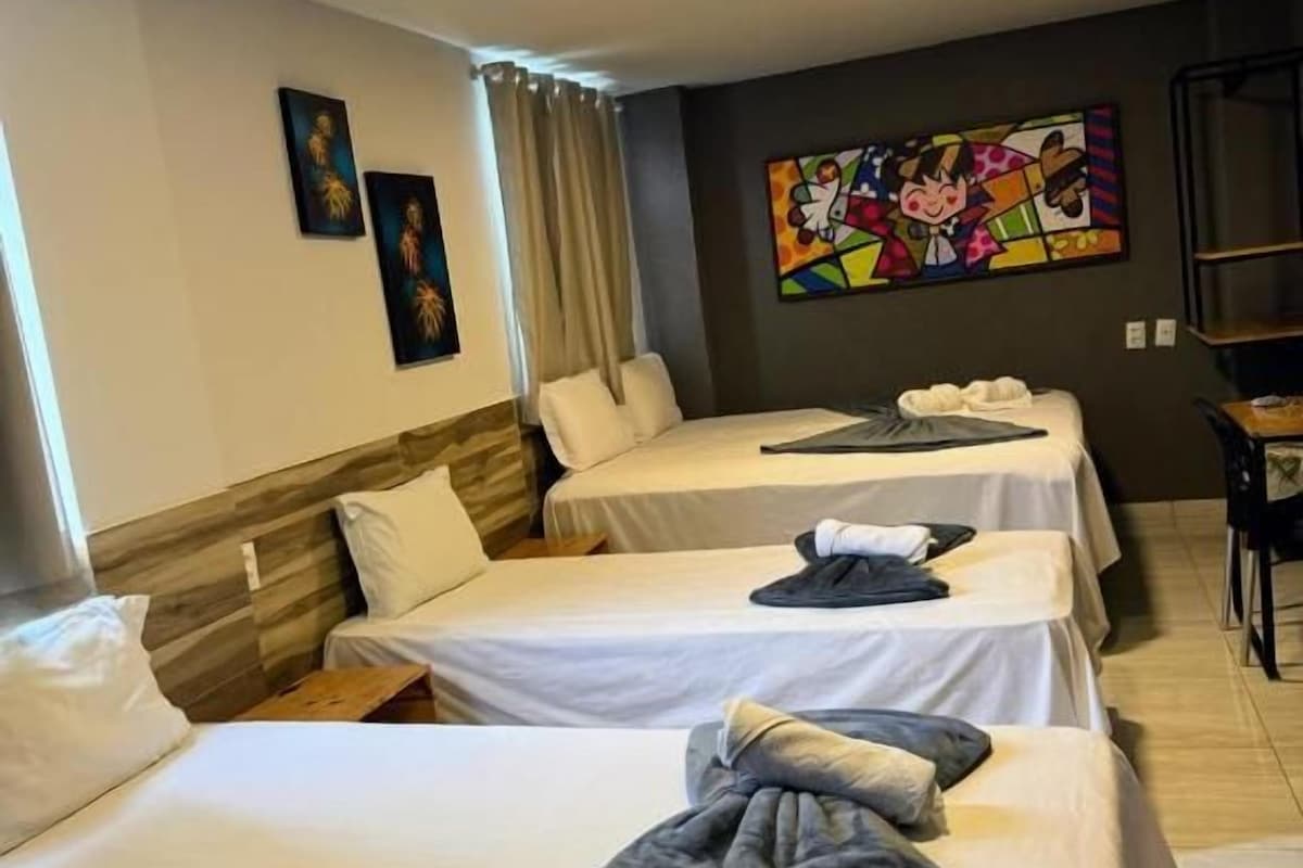 A hotel room with three beds, a large window with curtains, and a colorful abstract painting on the wall.