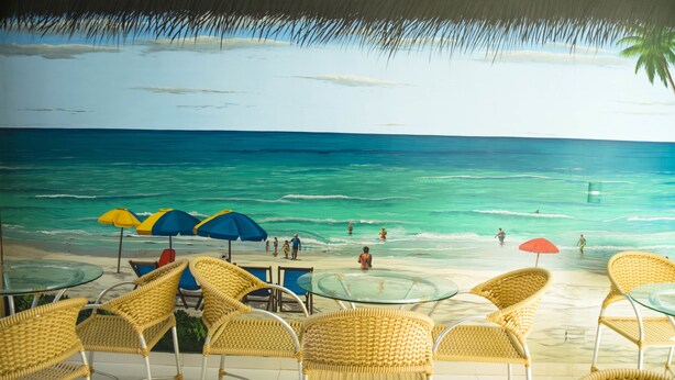 A beachside restaurant with wicker chairs and tables, overlooking the ocean.