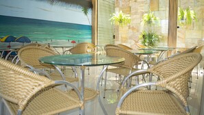 A beachside restaurant with wicker chairs and glass tables, overlooking the ocean.