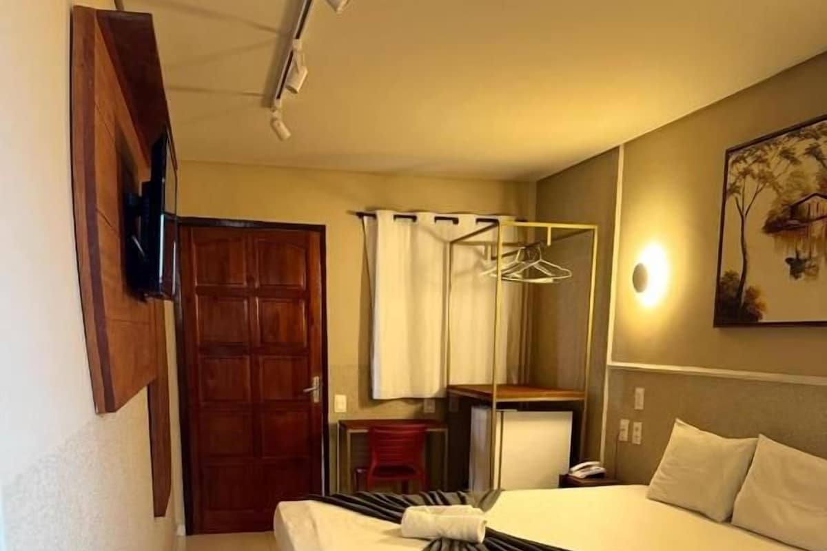 A hotel room with two beds, a wardrobe, a mirror, and a painting on the wall.