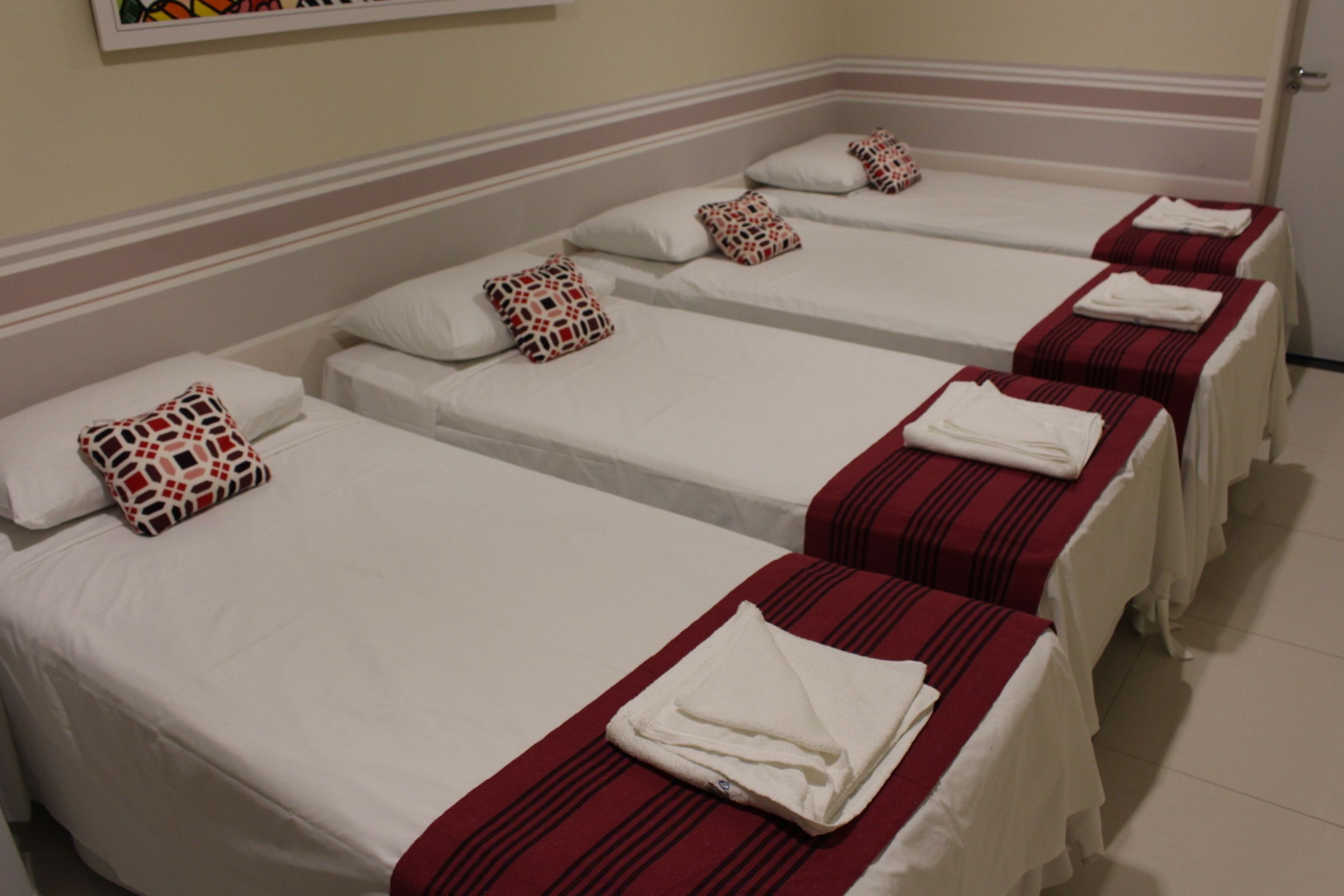 A row of four single beds with white linens and red-striped bedspreads, each with a patterned pillow.