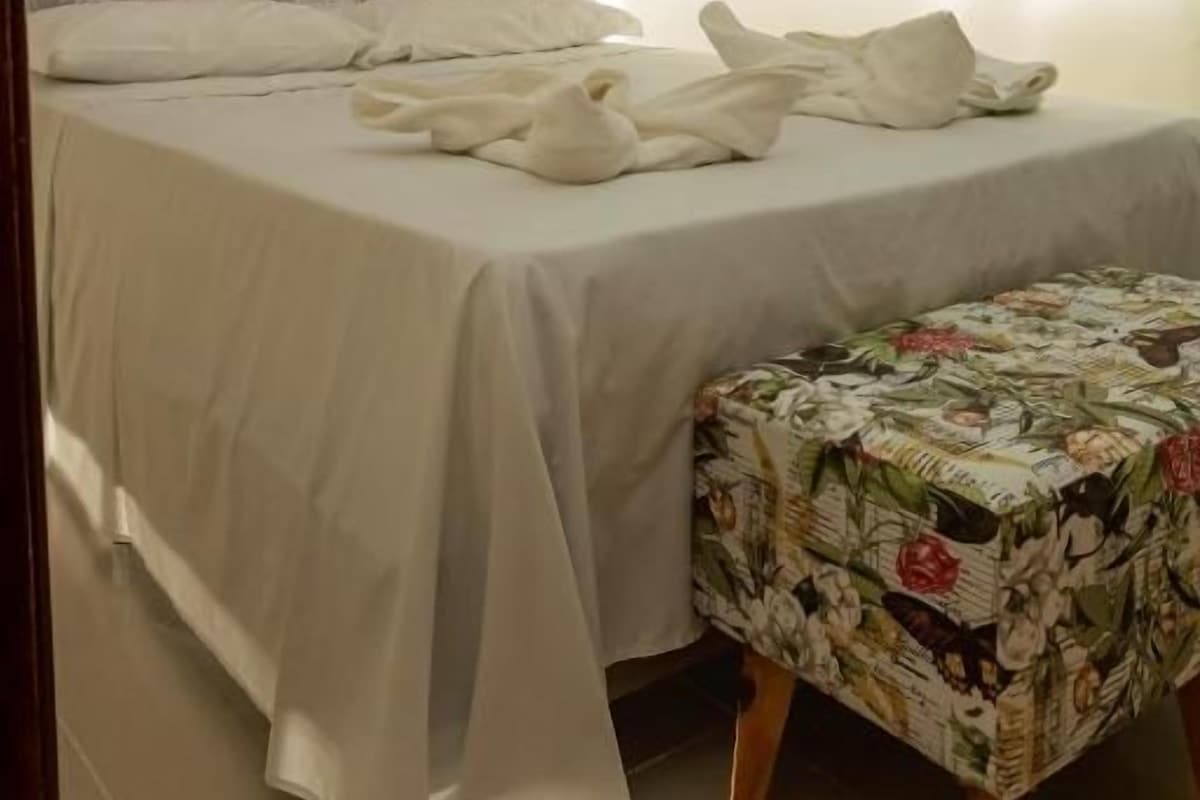 A hotel room with a bed, a bench, a TV, and curtains.