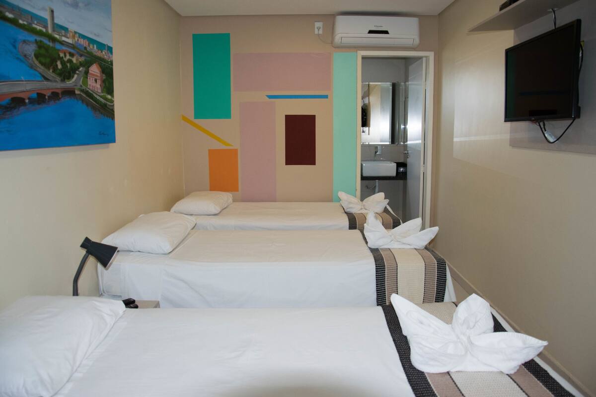 A hotel room with three beds, a painting on the wall, and a TV mounted on the wall.