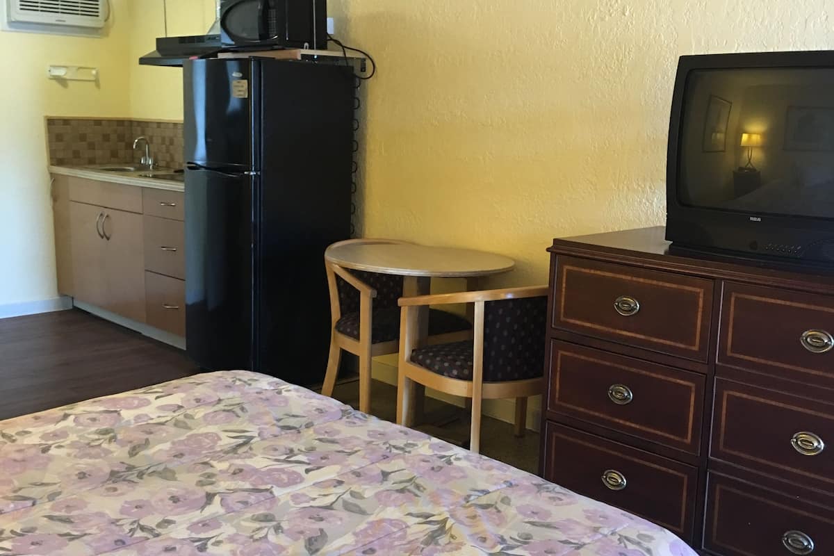 A compact room with a bed, a small dining table, a refrigerator, a microwave, and a television.