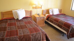 Dos camas individuales con ropa de cama estampada, una mesita de noche con lámpara y una ventana con persianas.