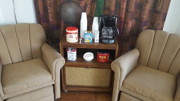 Una sala de estar con dos sillones color beige, una mesa de centro y una estantería con diversos objetos, incluyendo una cafetera, tazas y recipientes.