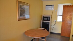 Una habitación pequeña con una mesa y sillas de madera, un cuadro en la pared, un microondas y una puerta con ventana.
