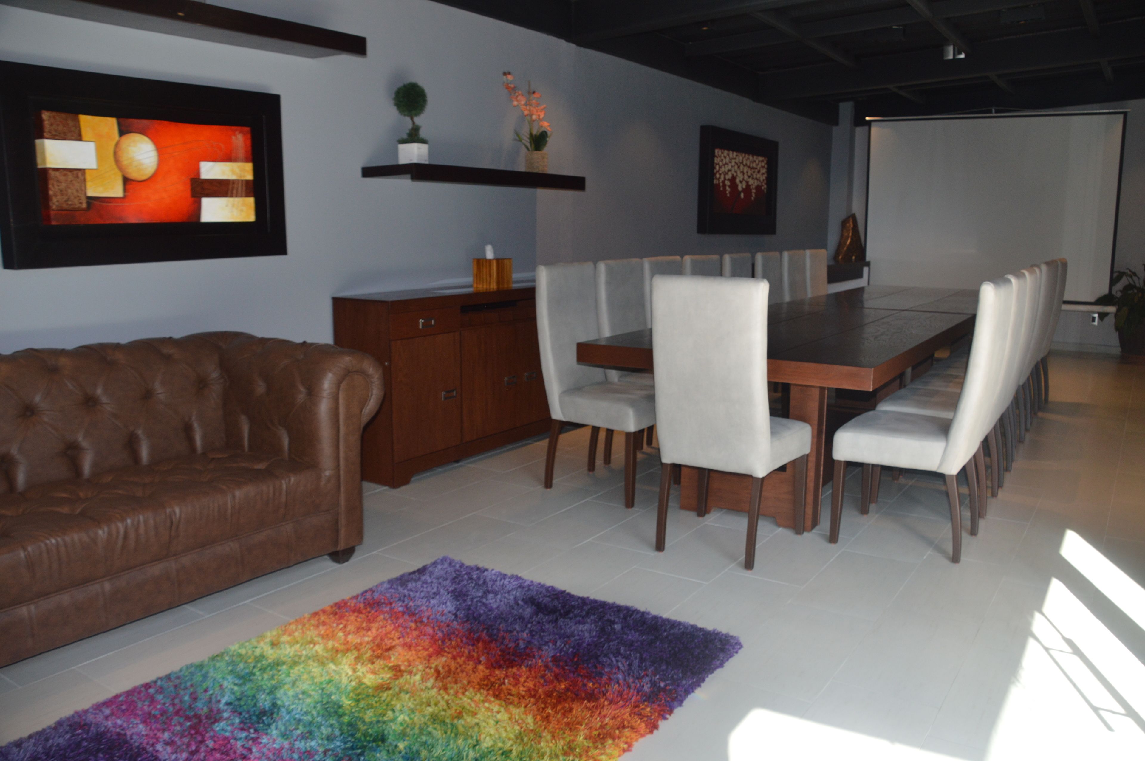Un comedor moderno con una mesa de madera alargada, sillas tapizadas blancas y un sofá de cuero marrón.