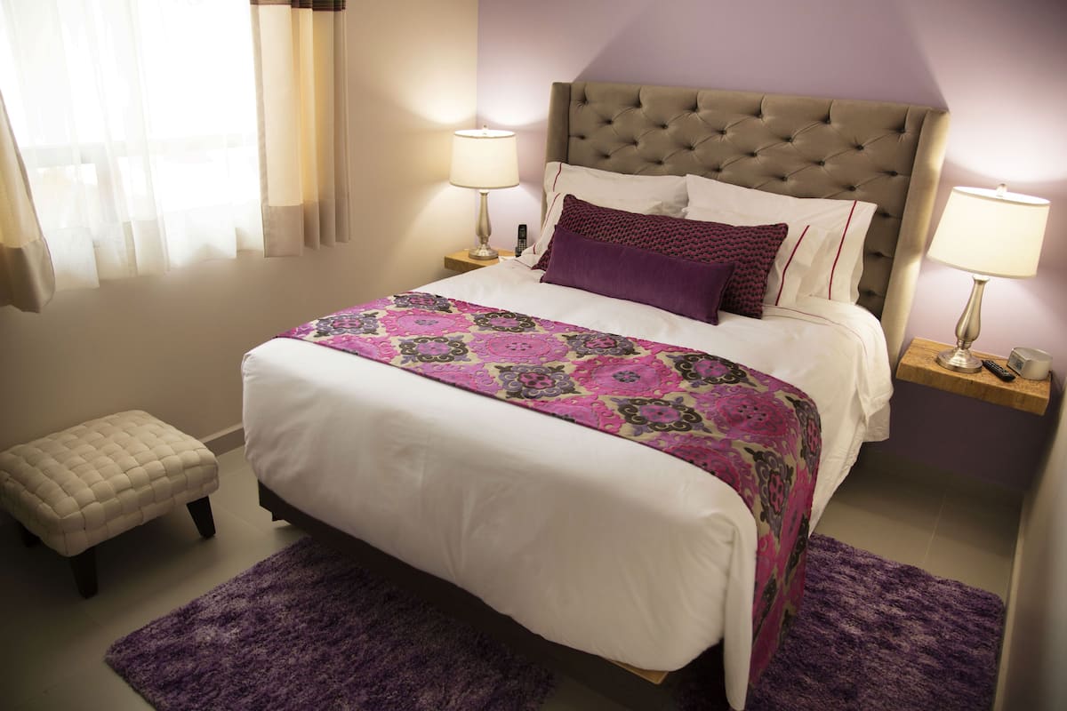 A neatly made bed with a patterned bedspread, a tufted headboard, and two bedside lamps.
