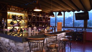 A bar area with a stone counter, metal chairs, and a variety of bottles and glasses.