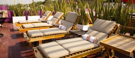 Un área de descanso en la azotea con sillones de madera, cojines color beige y una mesa de madera.