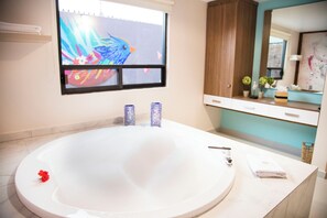 A modern bathroom with a large bathtub, a window with artwork, and a vanity with a mirror and cabinets. - La Morada Tepotzotlan Boutique & Spa (Tepotzotlán)