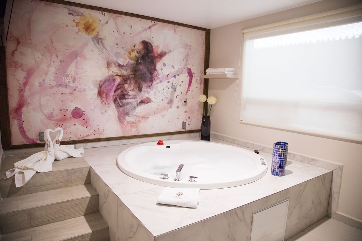 A modern bathroom with a large bathtub, marble countertops, and a decorative abstract painting on the wall.