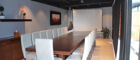 Una sala de conferencias moderna con una larga mesa de madera, sillas blancas y una planta en maceta.