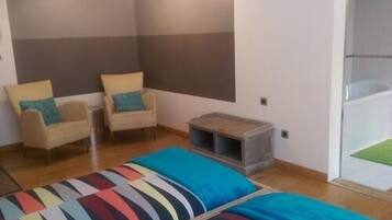 A room with two beds, two chairs, a small table, and a shower area.