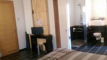 Een slaapkamer met een bed, een bureau met een computer, een douche en een toilet.