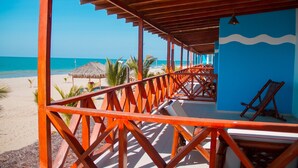 Una estructura frente a la playa, con techo de madera y barandillas anaranjadas, con vista al océano.