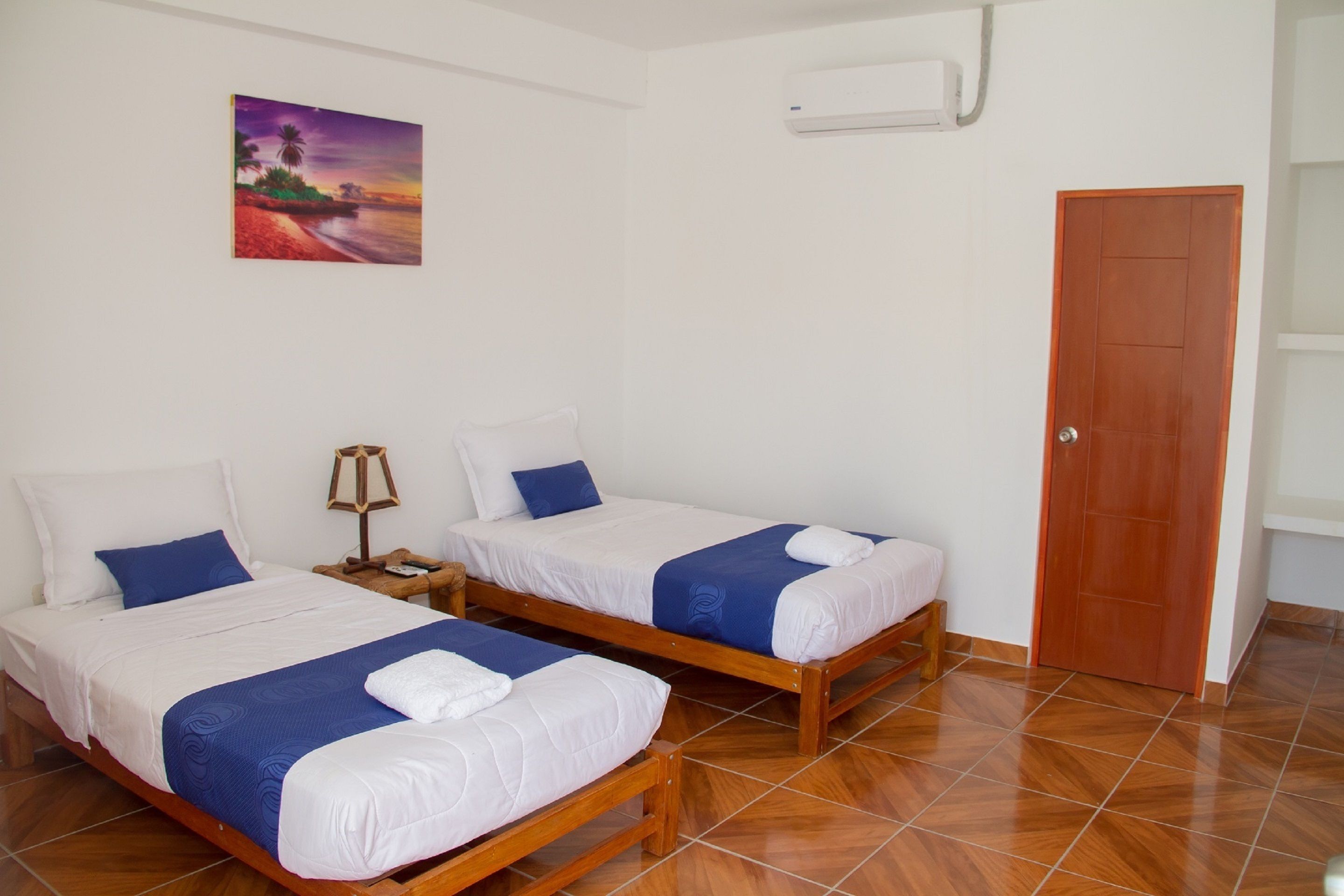 Una habitación con dos camas de madera, ropa de cama blanca y detalles azules.