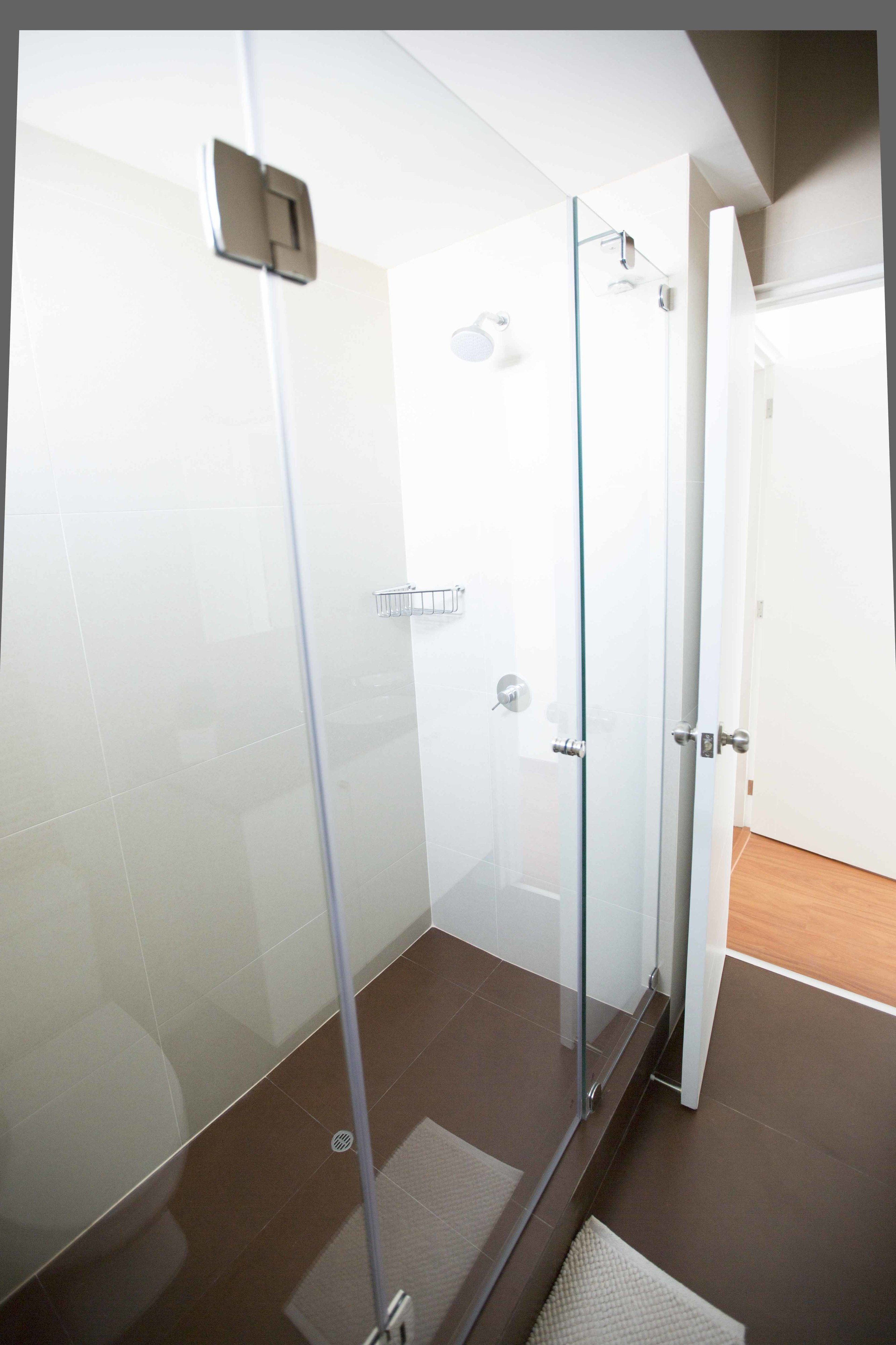 Une salle de bain moderne avec une douche à parois de verre, des carreaux blancs et un plancher en bois.