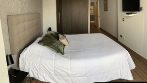 Una habitación de hotel con una cama grande, un armario, un televisor montado en la pared y un pasillo que da a otras habitaciones.