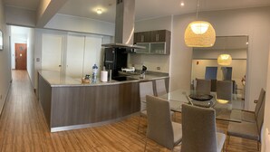 Una cocina moderna con una isla central, un comedor con mesas y sillas de vidrio, y un pasillo que conduce a otra habitación.
