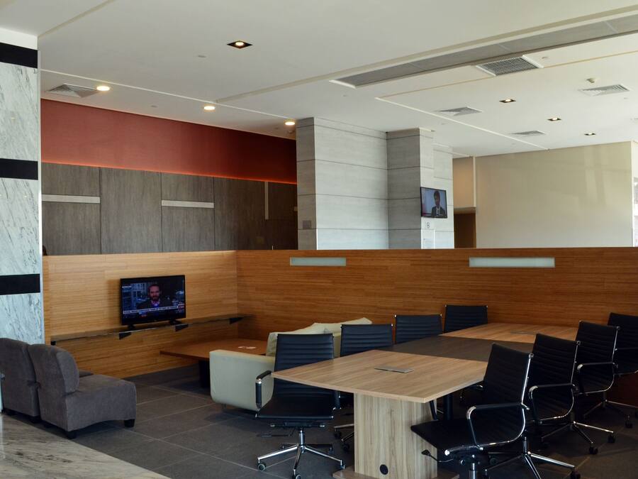 A modern conference room with a large table, black chairs, a TV screen, and a wooden accent wall.