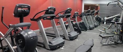 Un gimnasio con cintas de correr, una banca y máquinas de pesas.