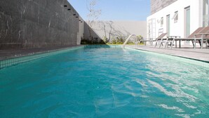A swimming pool with clear blue water, surrounded by a concrete wall and a building with a modern design. - Hotel Casa Inn Business Irapuato (Irapuato)