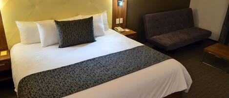 Ein Hotelzimmer mit einem großen Bett, einem Nachttisch mit Lampe, einer Couch und einer Wandleuchte.