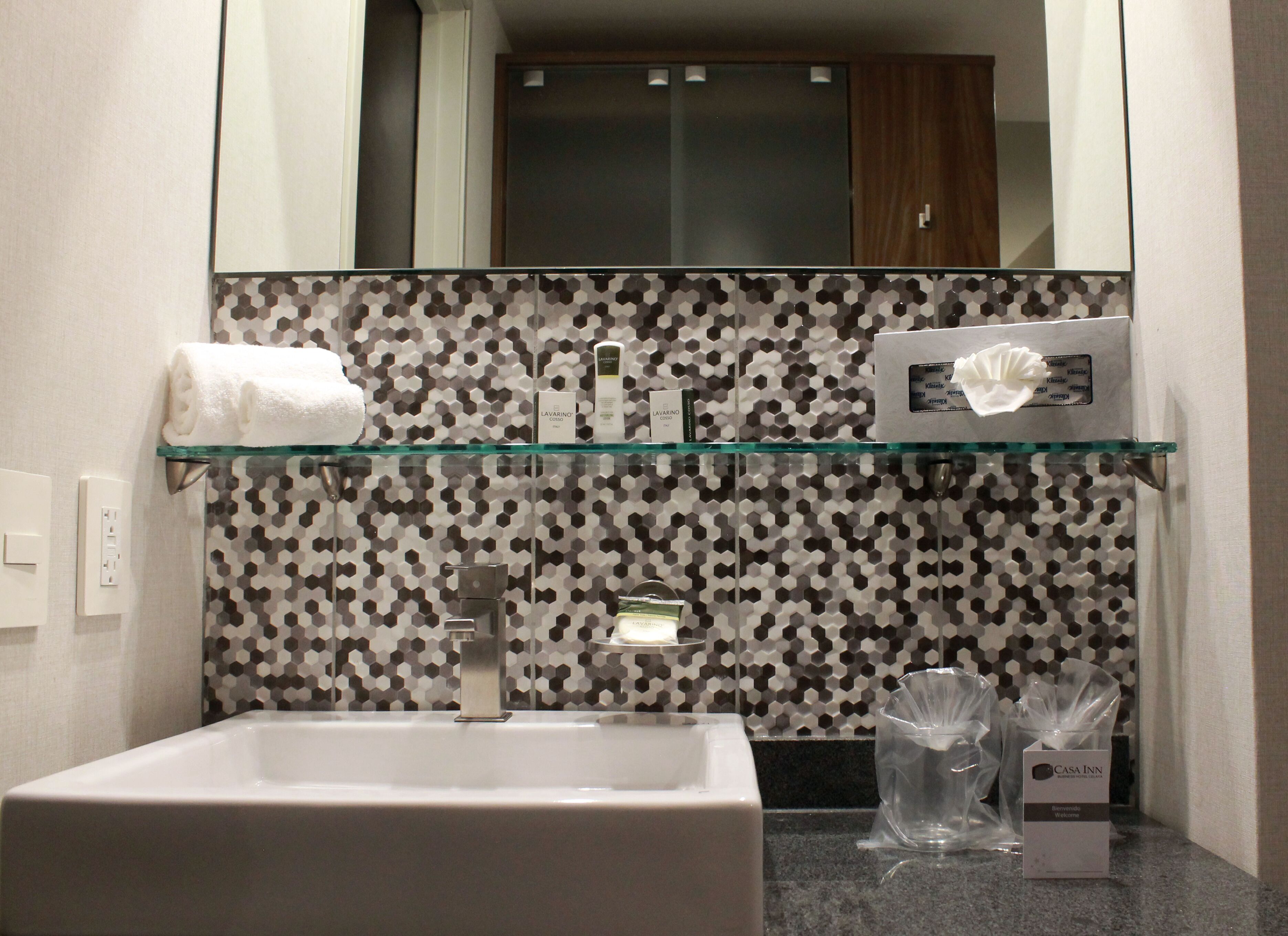 A bathroom with a glass shelf holding toiletries, a white sink, and a mirror above.