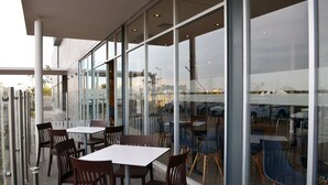 An outdoor seating area with tables and chairs, large windows, and a view of parked cars. - Hotel Casa Inn Business Irapuato (Irapuato)