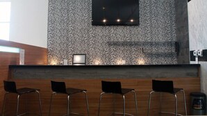A modern bar area with a patterned wall, a flat-screen TV, and three bar stools. - Hotel Casa Inn Business Irapuato (Irapuato)