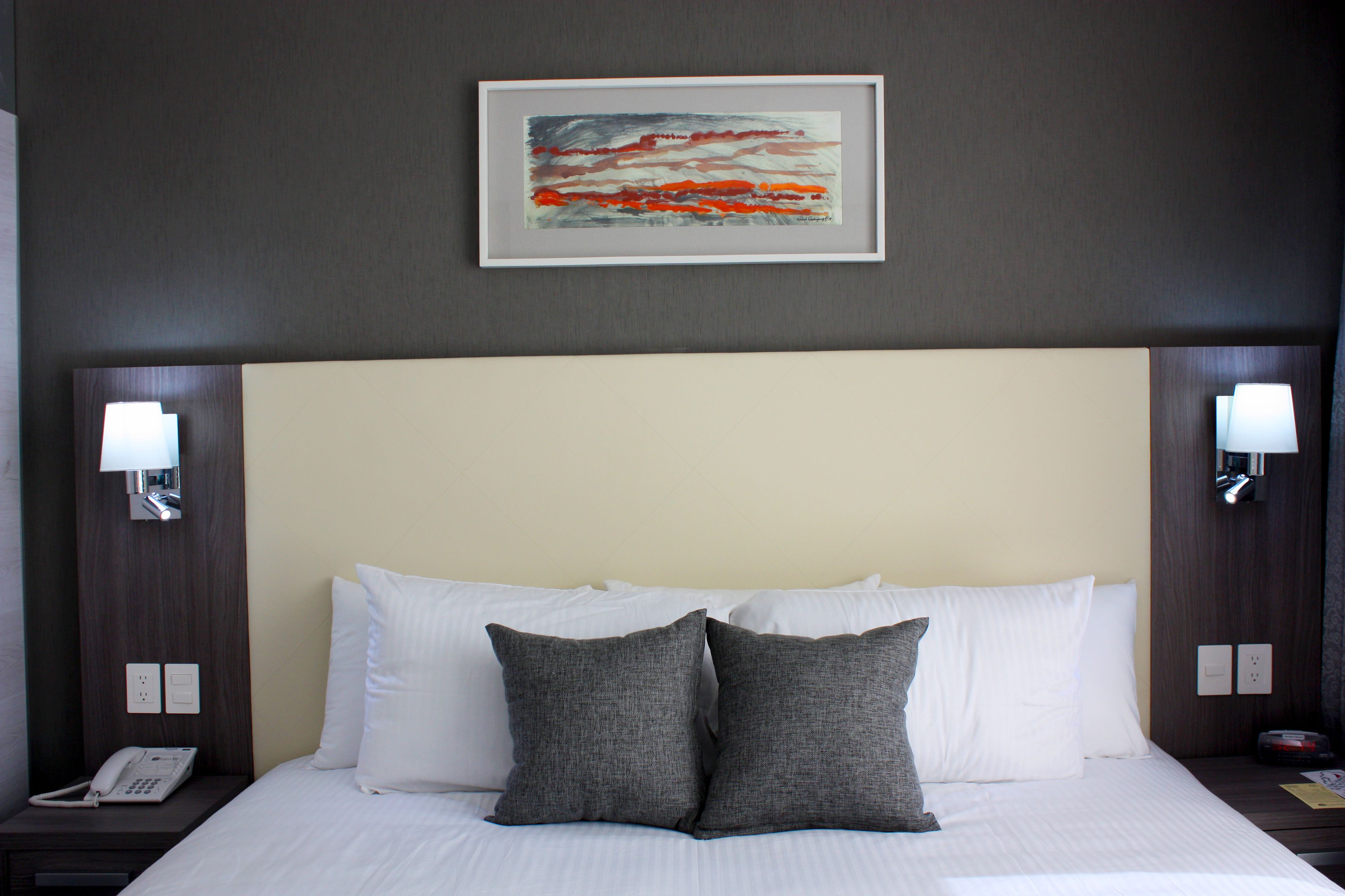 A hotel room with a large bed, two pillows, a framed artwork above the bed, and bedside lamps.