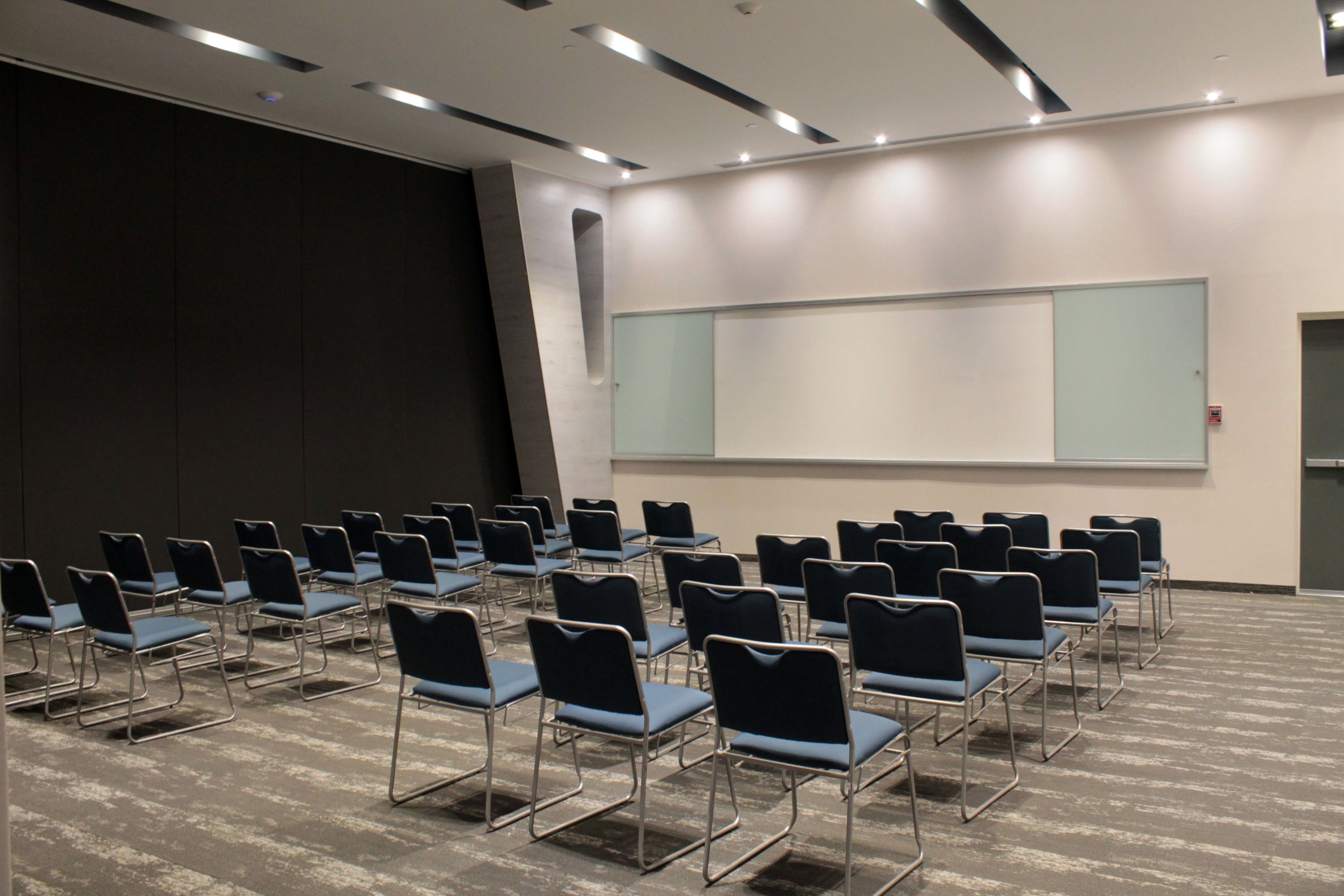 A conference room with rows of chairs, a large projection screen, and a door.