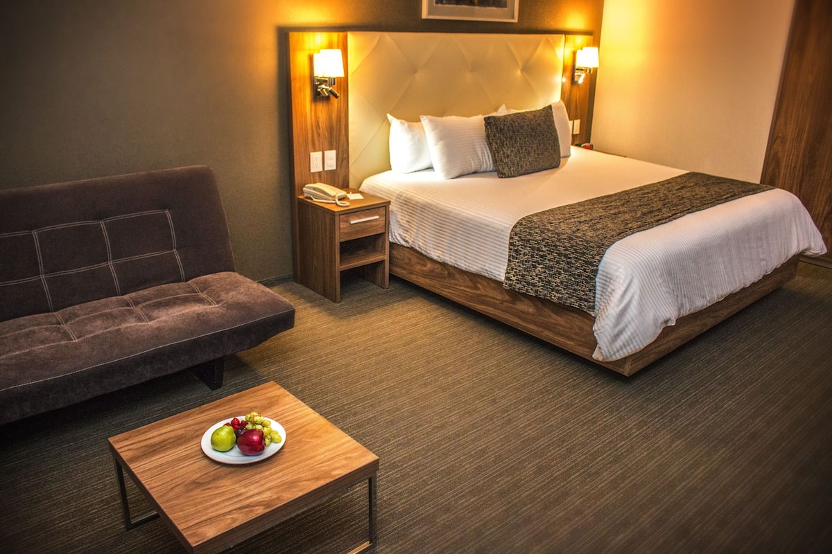 Een hotelkamer met een bed, een slaapbank, een nachtkastje met een lamp en een klein tafeltje met fruit.