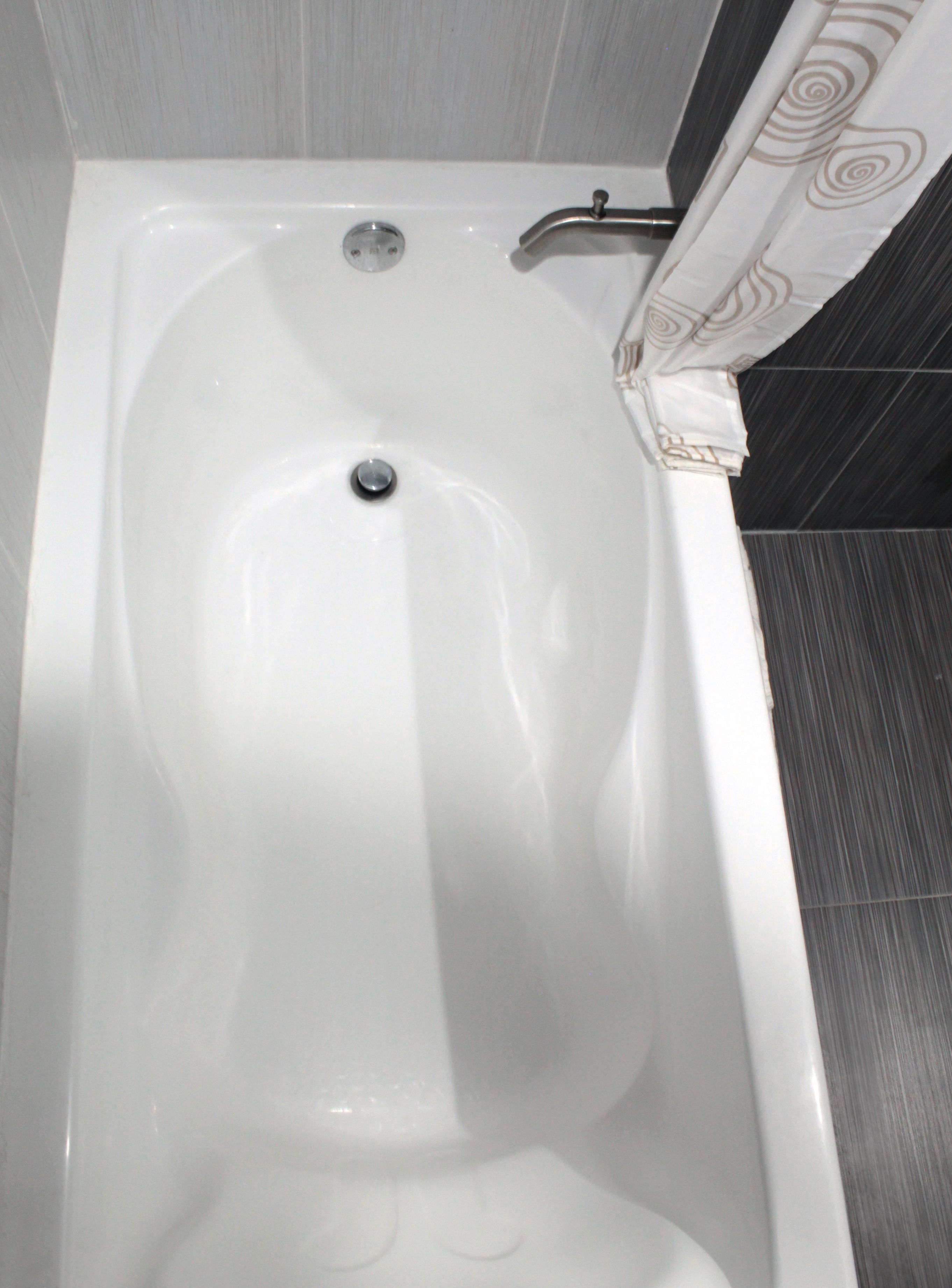 Una bañera blanca con un solo grifo y desagüe, frente a una pared con azulejos.