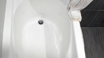 Ett vitt badkar med ett enda blandare och avlopp, placerat framför en kaklad vägg.