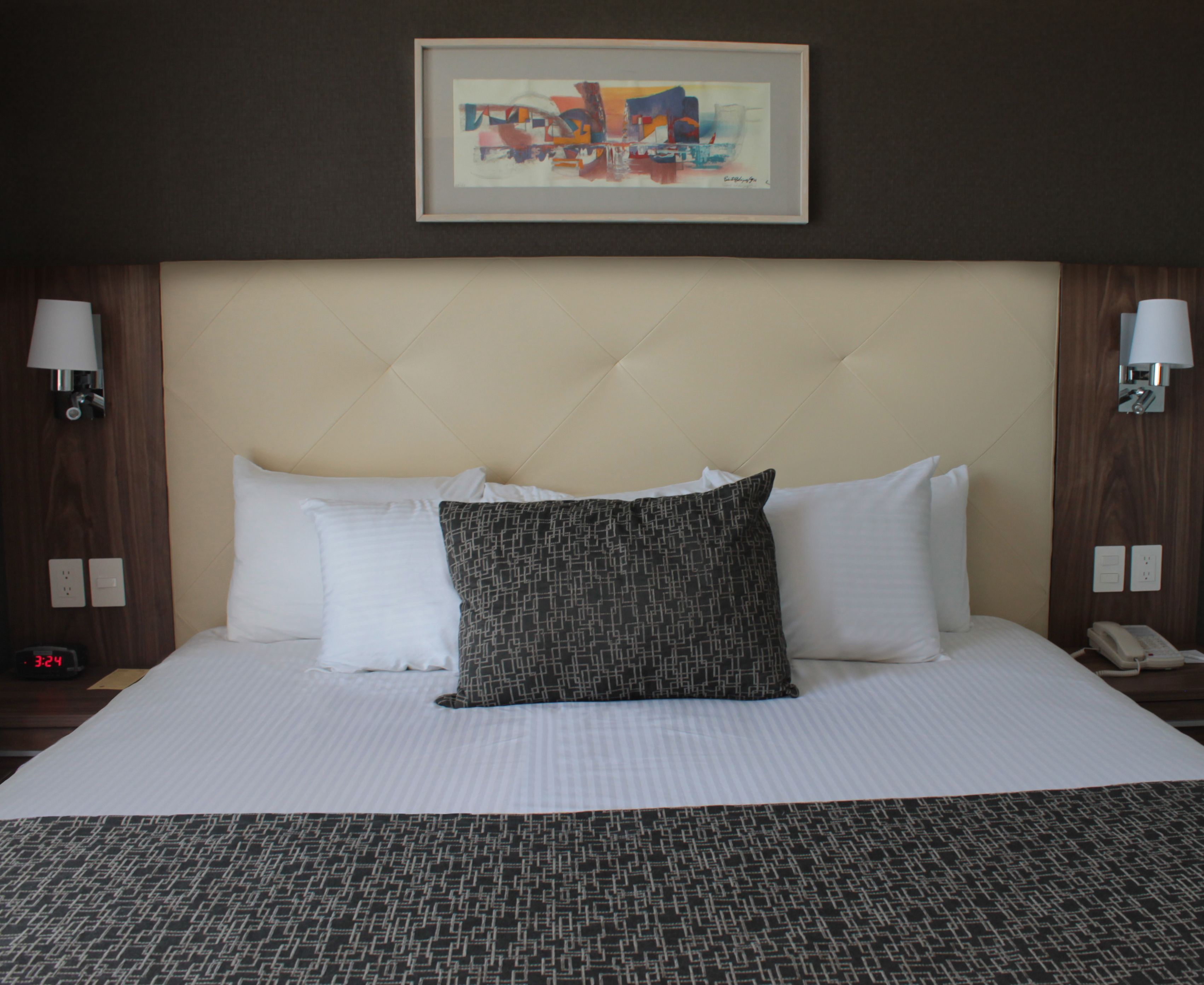 Quarto de hotel com uma cama grande, duas luminárias de cabeceira, um quadro abstrato emoldurado e telefone ao lado da cama.
