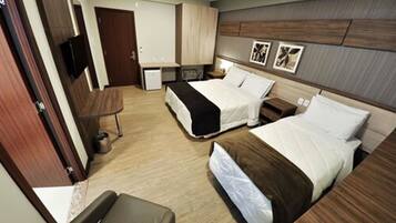 A hotel room with two beds, a desk, a chair, a small table, and a TV.