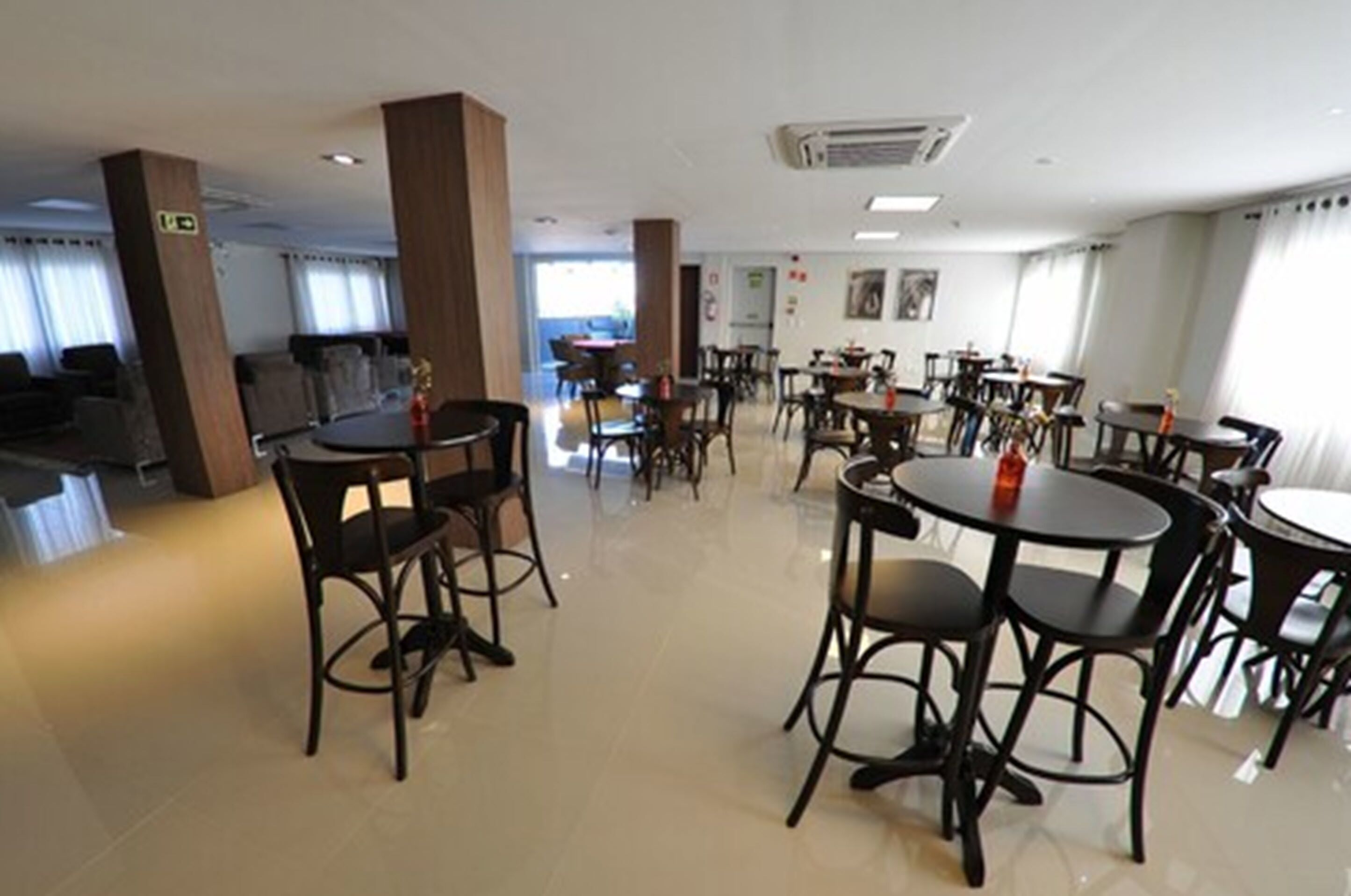 Un comedor de hotel con mesas y sillas redondas, un ventanal grande y una señal de salida visible.