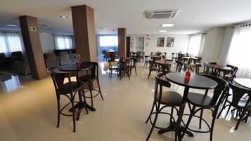 Un comedor de hotel con mesas y sillas redondas, un ventanal grande y una señal de salida visible.
