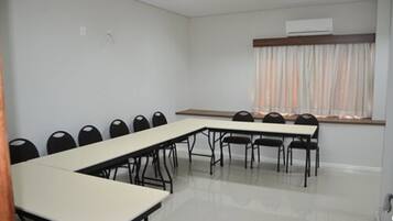 A conference room with a long table and chairs, a window with curtains, and an air conditioning unit on the wall.