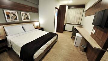 A hotel room with a bed, bedside tables, a desk, a chair, a TV, and artwork on the wall.