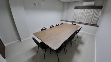 A conference room with a long table and chairs, a window with curtains, and an air conditioning unit on the wall.