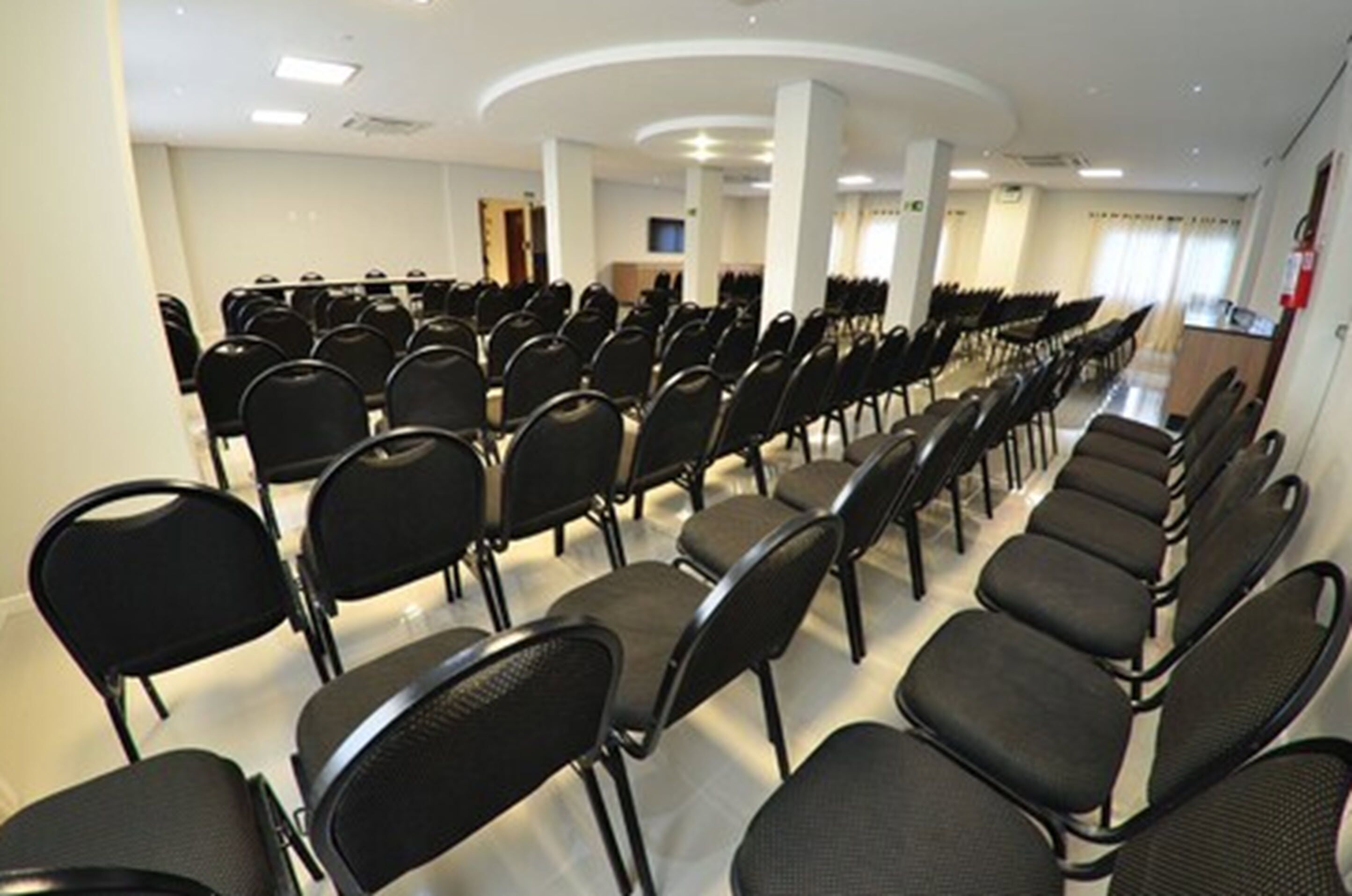 Un salón de conferencias con hileras de sillas negras y un techo blanco.