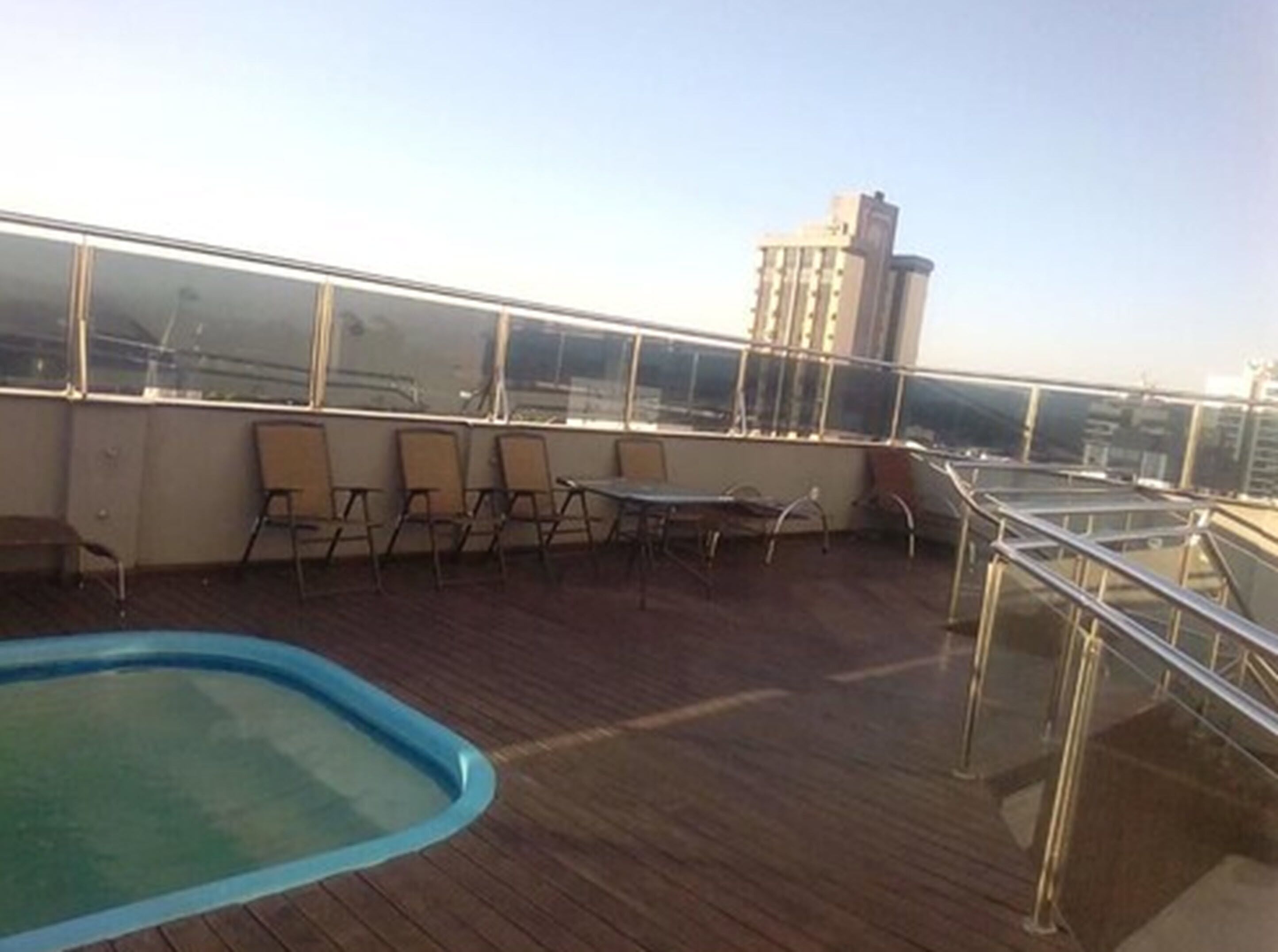 Um terraço no telhado com piscina, espreguiçadeiras e guarda-corpo de vidro.