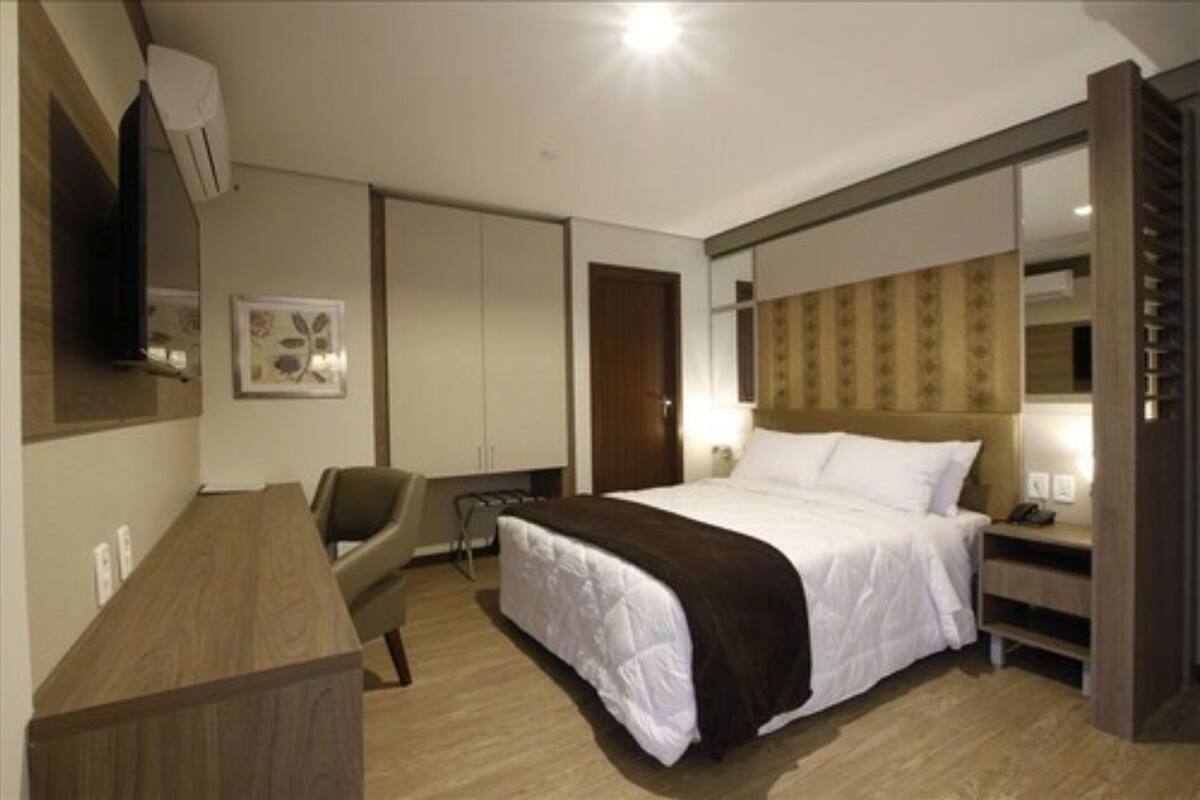 Una habitación de hotel con cama, mesita de noche, silla, armario y espejo.