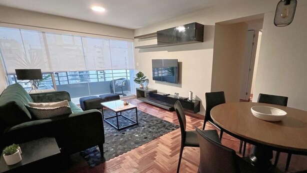 A modern living room with a sofa, coffee table, and dining table. - MLA apartments - Alcanfores (Lima)