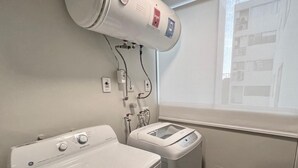 A laundry room with a front-loading washer and dryer, a water heater, and a window with a view of a building. - MLA apartments - Alcanfores (Lima)